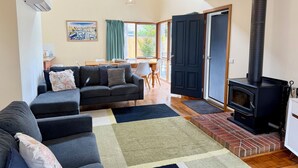 A living room with a sofa, a rug, a fireplace, and a dining area with a table and chairs. - Beach Life on Price: 2  BR, 1  BA Townhouse in Torquay, Sleeps 8 (Torquay)