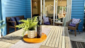 A blue exterior wall, a wooden deck, a table with a bottle and plants, and wicker chairs with cushions. - Beach Life on Price: 2  BR, 1  BA Townhouse in Torquay, Sleeps 8 (Torquay)