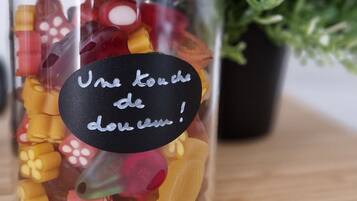 A glass jar filled with colorful gummy candies, with a label that reads "Une touche de douceur!" on a wooden surface with a potted plant in the background.