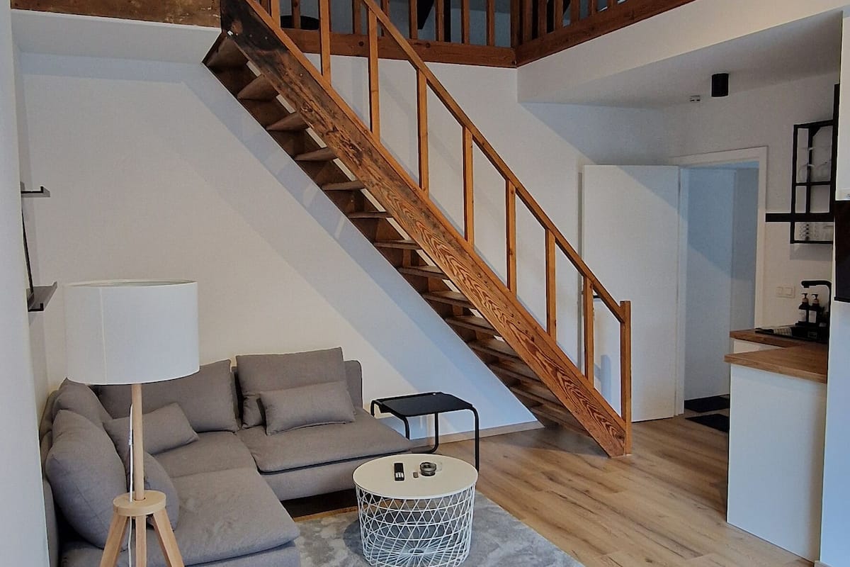Een moderne woonkamer met een houten trap, een grijze bank, een salontafel en een lamp.