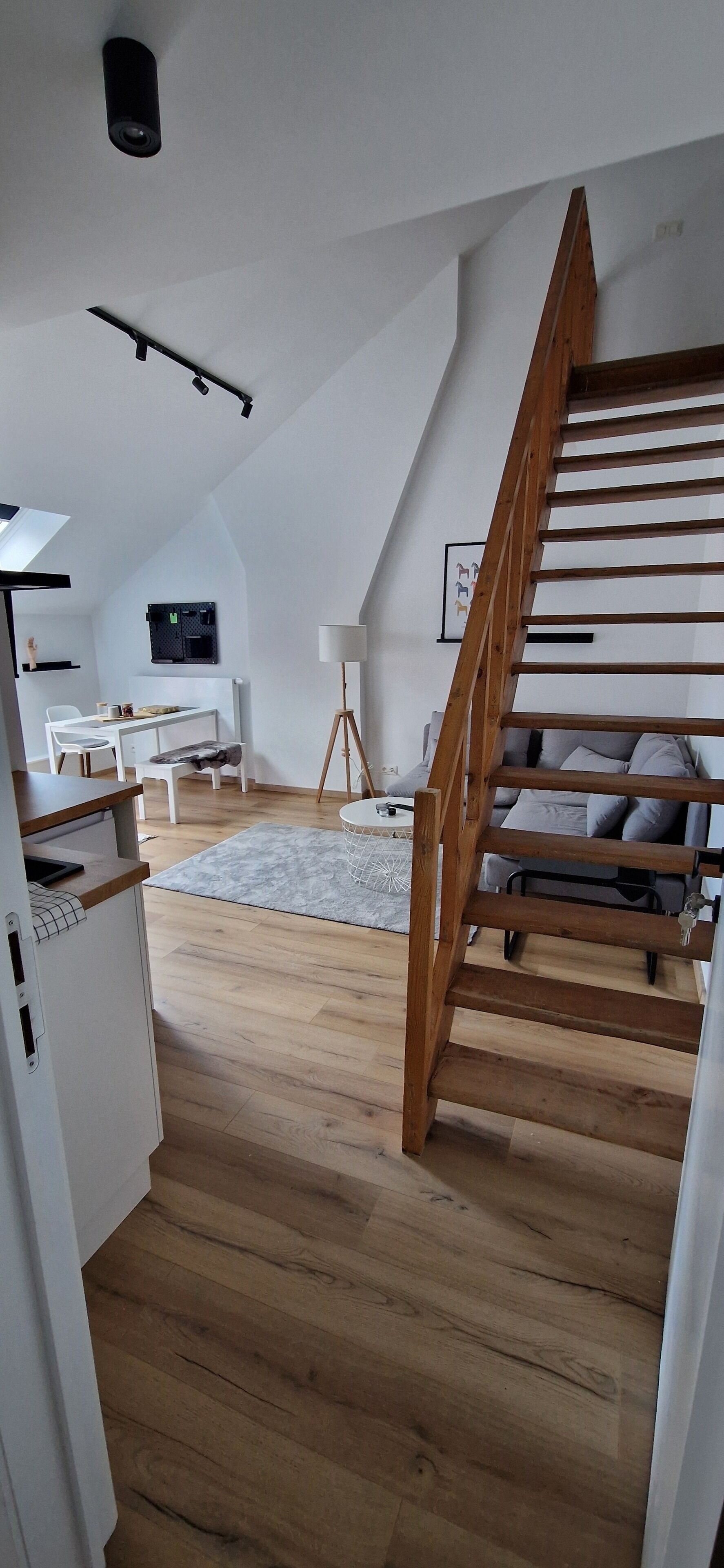 A loft-style room with a wooden staircase, a dining area with a white table and chairs, and a small white cabinet.
