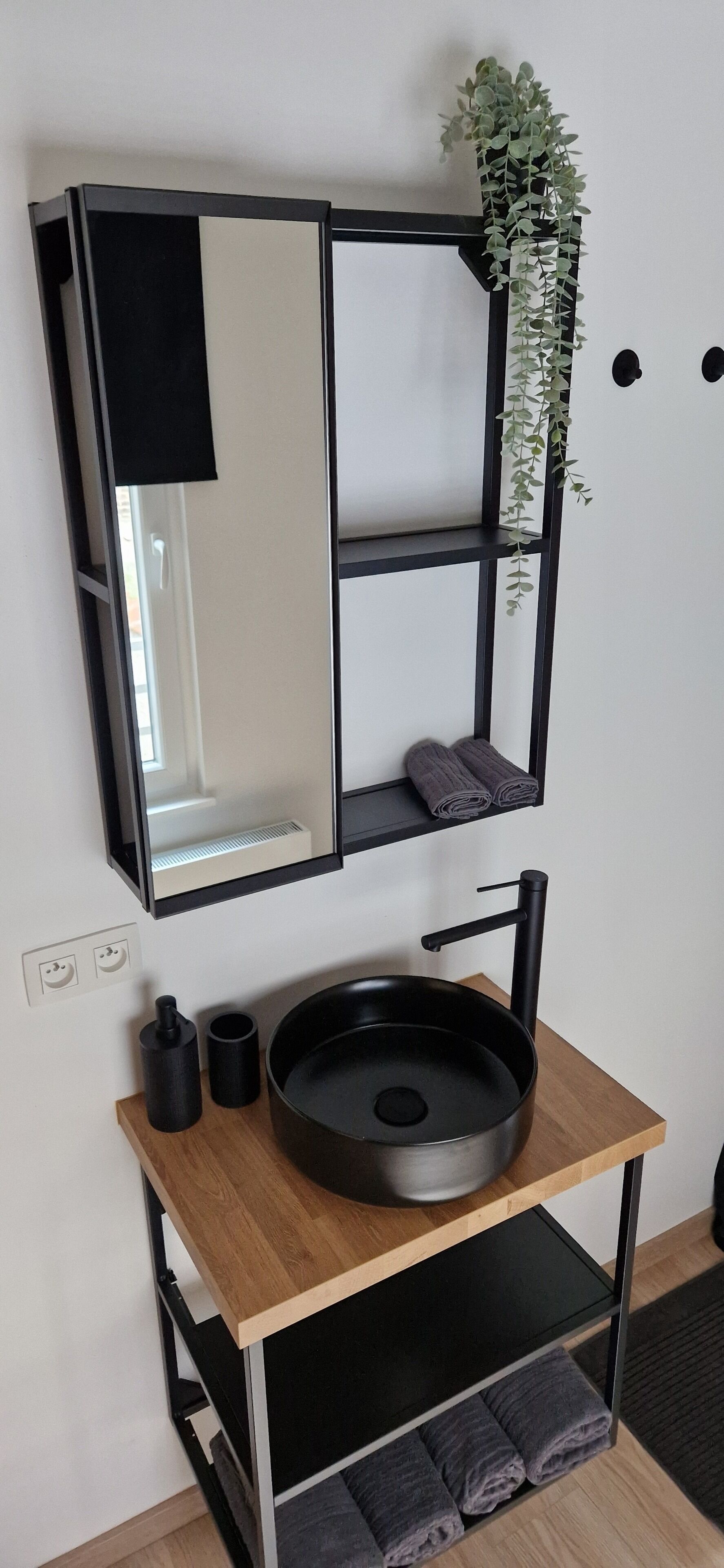 Un baño moderno con un espejo de marco negro, un lavabo redondo y un mueble de tocador de madera.