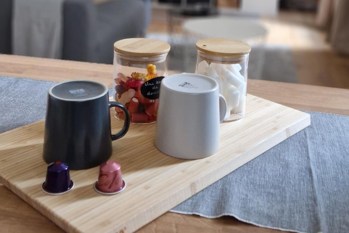 Een houten tafel met een dienblad waarop twee mokken, een potje met snoepjes en een klein bakje staan.