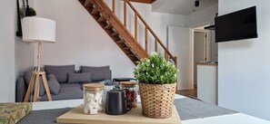 A living room with a wooden staircase, a grey sofa, a coffee table with jars and a plant, and a mounted TV. - Charleroi Cozy Home (Charleroi)