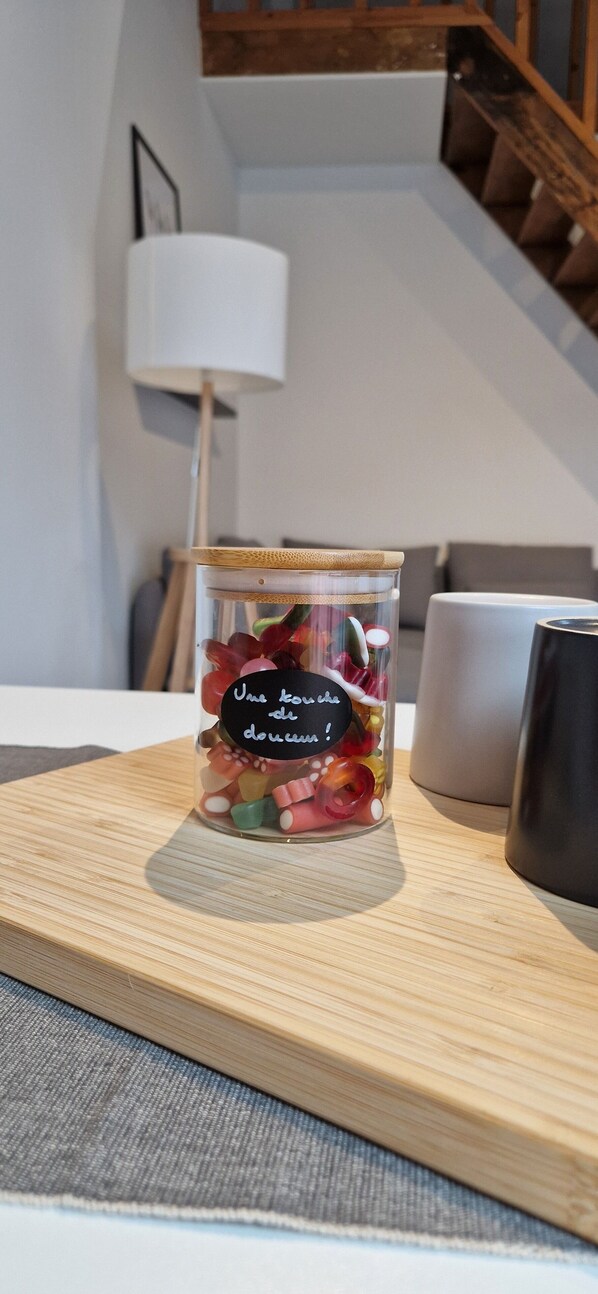 A glass jar with a label on a wooden table in a room with a staircase and a lamp in the background. - Charleroi Cozy Home (Charleroi)