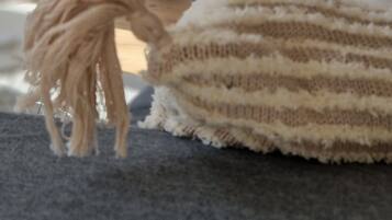En närbild på ett stickat föremål med en tofs, placerat på en grå soffa.