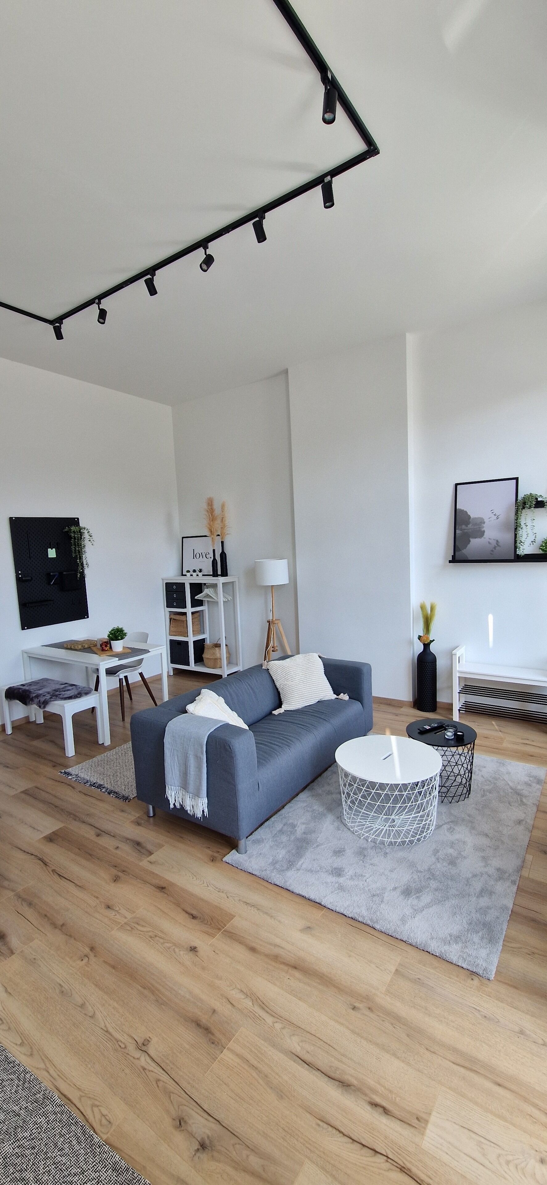 Ein modernes Wohnzimmer mit einem grauen Sofa, einem runden Couchtisch, einem Fernseher und einem Bücherregal.