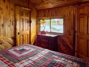 Une pièce en bois avec un lit, une commode et une fenêtre où est posé un parapluie.