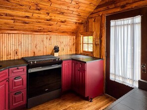 Une cuisine avec des murs en bois, un plan de travail rouge et une cuisinière.