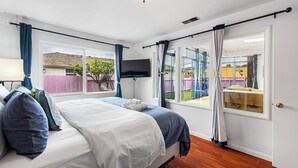 A bedroom with a bed, a TV mounted on the wall, and a window with curtains.