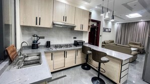 A modern kitchen with a central island, bar stools, and a dining area with a sofa and chairs. - GARDEN PARK HOUSE (Kigali)