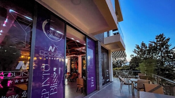A modern lounge area with a glass facade, outdoor seating, and a view of the sky. - GARDEN PARK HOUSE (Kigali)