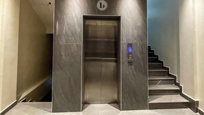 A modern elevator with a marble wall and a digital display, leading to a staircase. - GARDEN PARK HOUSE (Kigali)
