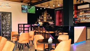 A bar area with orange chairs and tables, a TV mounted on the wall, and a variety of bottles on shelves. - GARDEN PARK HOUSE (Kigali)