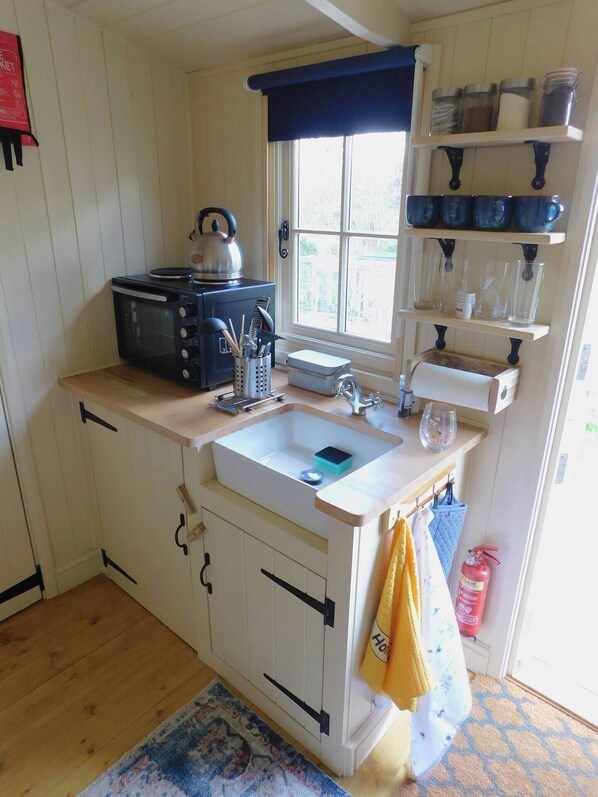 Una cocina compacta con un lavamanos, hervidor y estantes de almacenamiento.