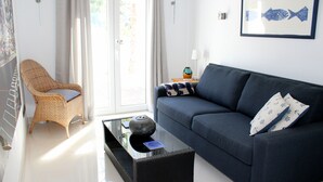 A living room with a sofa, a wicker chair, a glass coffee table, and a door leading outside. - Luxury villa with stunning sea views, walking distance from El Portet beach. (Teulada)