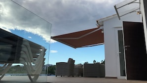 A modern outdoor area with a glass balustrade, wicker furniture, and a clear view of the sky. - Luxury villa with stunning sea views, walking distance from El Portet beach. (Teulada)