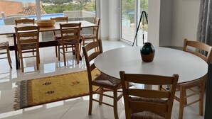 A dining area with a round table and wooden chairs, large windows with a view of the sea and mountains, and a framed picture on the wall. - Luxury villa with stunning sea views, walking distance from El Portet beach. (Teulada)