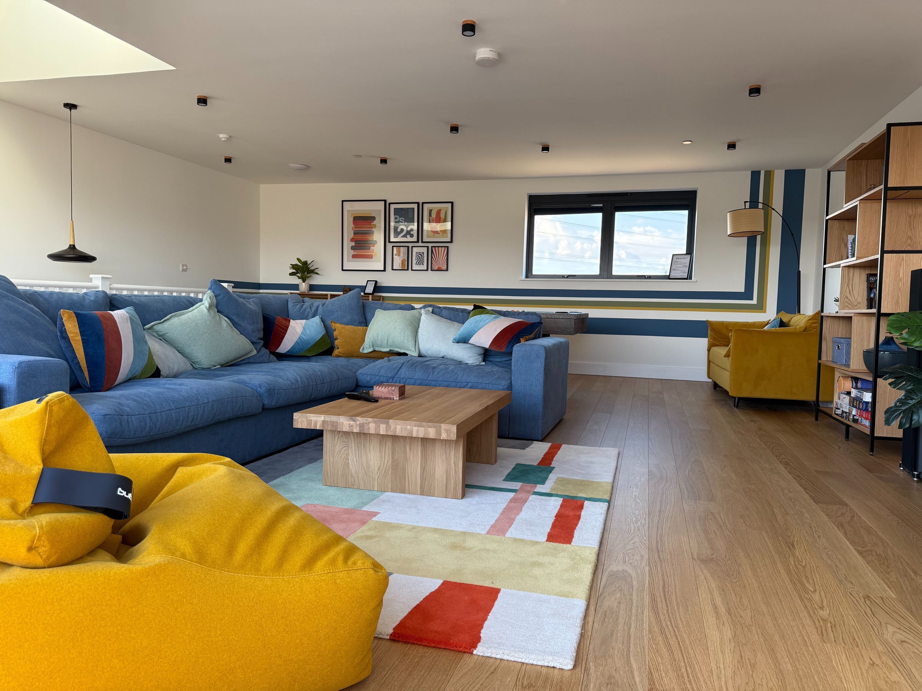 A modern living room with a blue sectional sofa, a yellow bean bag, and a wooden coffee table.