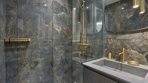 Een moderne badkamer met marmeren wanden, een douche met glazen wanden en een wastafel met gouden details.