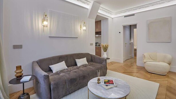 Een moderne woonkamer met een grijze bank, een ronde salontafel en een beige fauteuil.