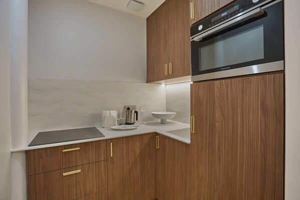 Cocina compacta con armarios de madera, horno empotrado y encimera blanca.