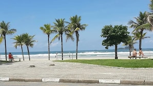 Ein gepflasterter Weg mit Bänken, Palmen und Blick auf das Meer.