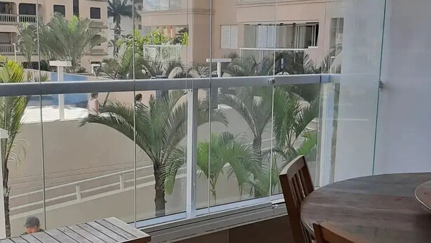 Ein Balkon mit Holztisch und -stühlen, einer Glastür und Blick auf Palmen und Gebäude.