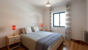 A bedroom with a bed, nightstands, a window with curtains, and a radiator. - Apartamento Ouri o by Acasadascasas (Mafra)