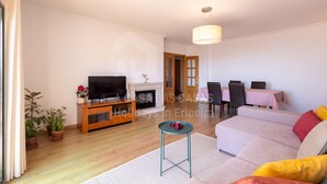 A living room with a sofa, television, fireplace, dining table, and chairs. - Apartamento Ouri o by Acasadascasas (Mafra)