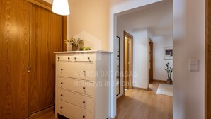A hallway with wooden flooring, a white dresser with drawers, a hanging light fixture, and a wooden door. - Apartamento Ouri o by Acasadascasas (Mafra)
