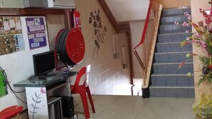 A hotel lobby with a staircase, a desk with a computer, a red chair, and a wall with a floral design. - Hotel O Malaysia Hotel (Sandakan)