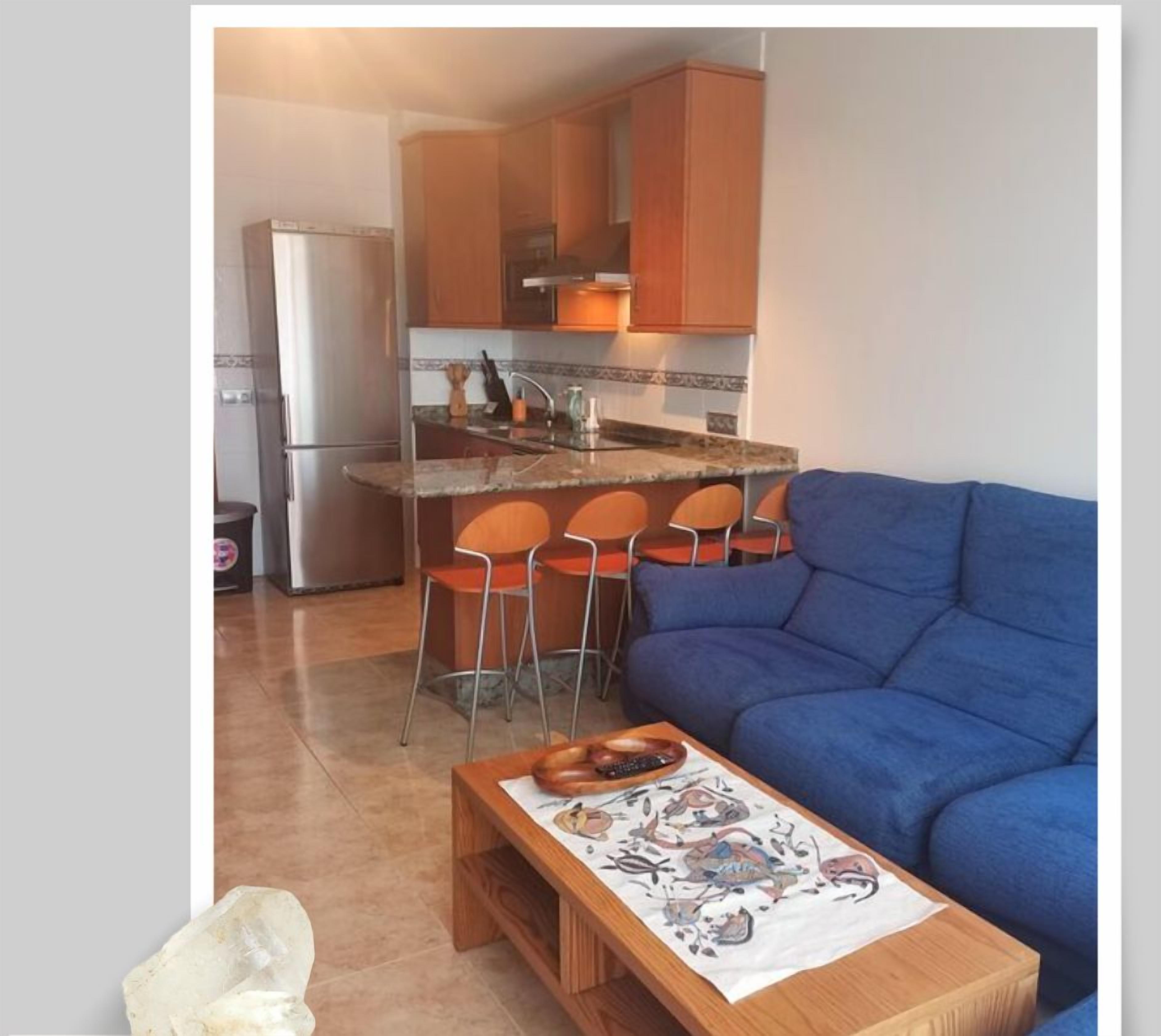 Un ambiente abitativo compatto con angolo cottura, un divano blu e un piccolo tavolo da pranzo.