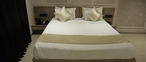 Una cama bien hecha con estructura de madera y ropa de cama blanca, una mesita de noche con lámpara y una pared con un panel decorativo.