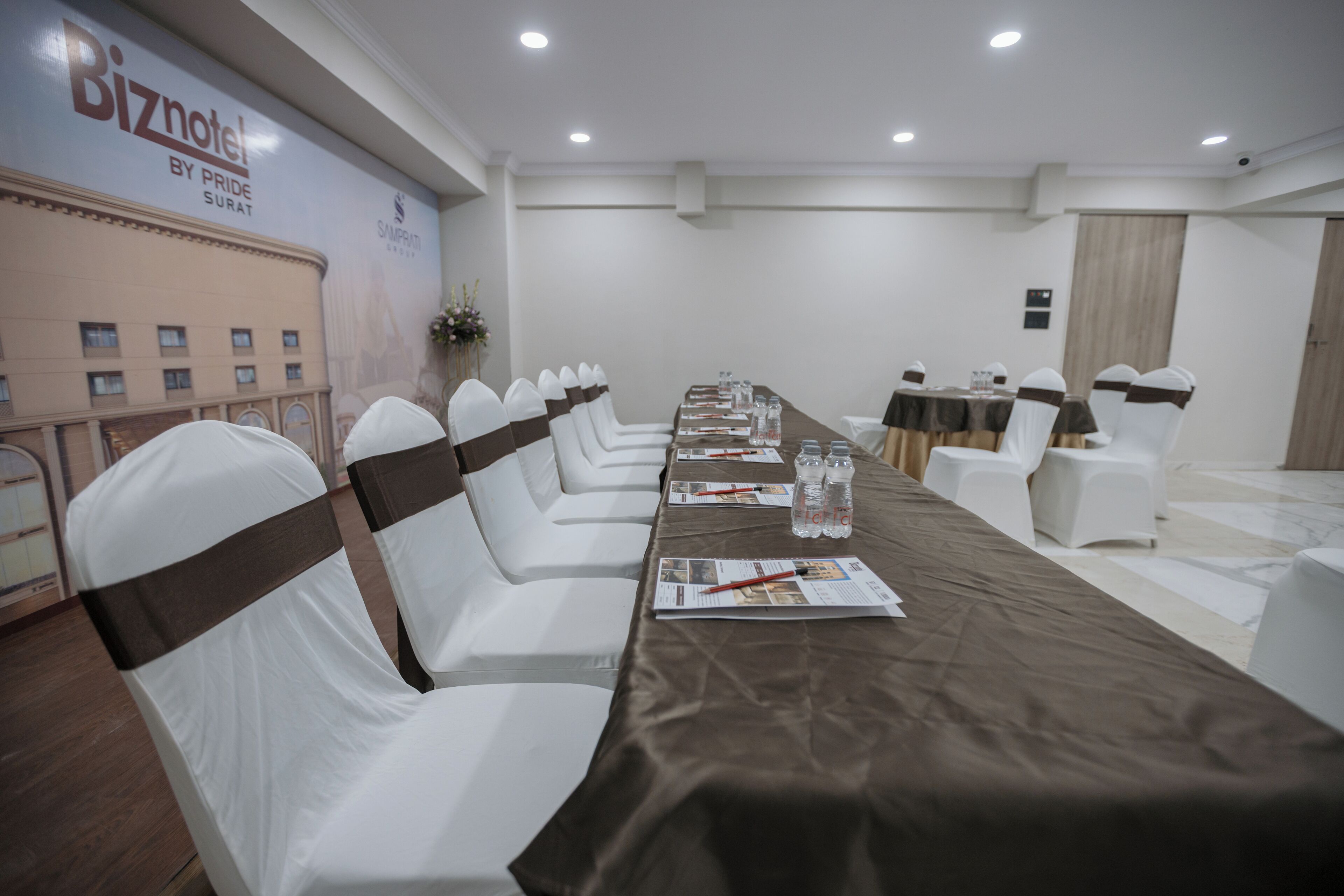 A conference room with a long table, white chairs with brown sashes, and a banner on the wall.