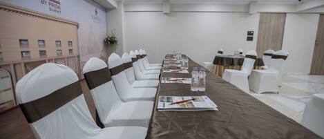 A conference room with a long table, white chairs with brown sashes, and a banner on the wall.