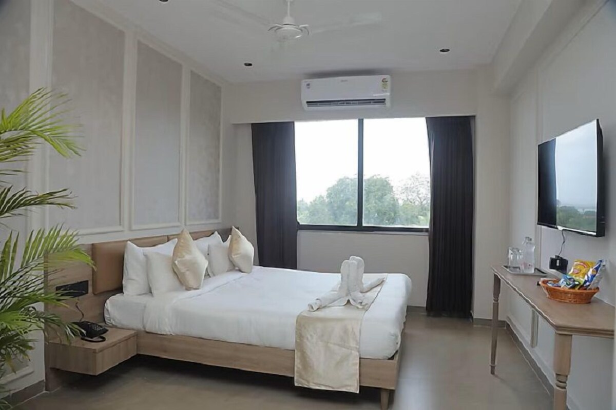 A hotel room with a bed, bedside table, TV, and an air conditioning unit.