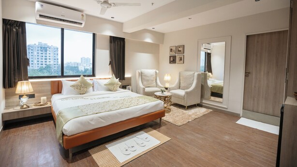 A modern hotel room with a large bed, a sitting area with chairs, a ceiling fan, an air conditioning unit, and a city view. - Biznotel by Pride Surat (Surat)