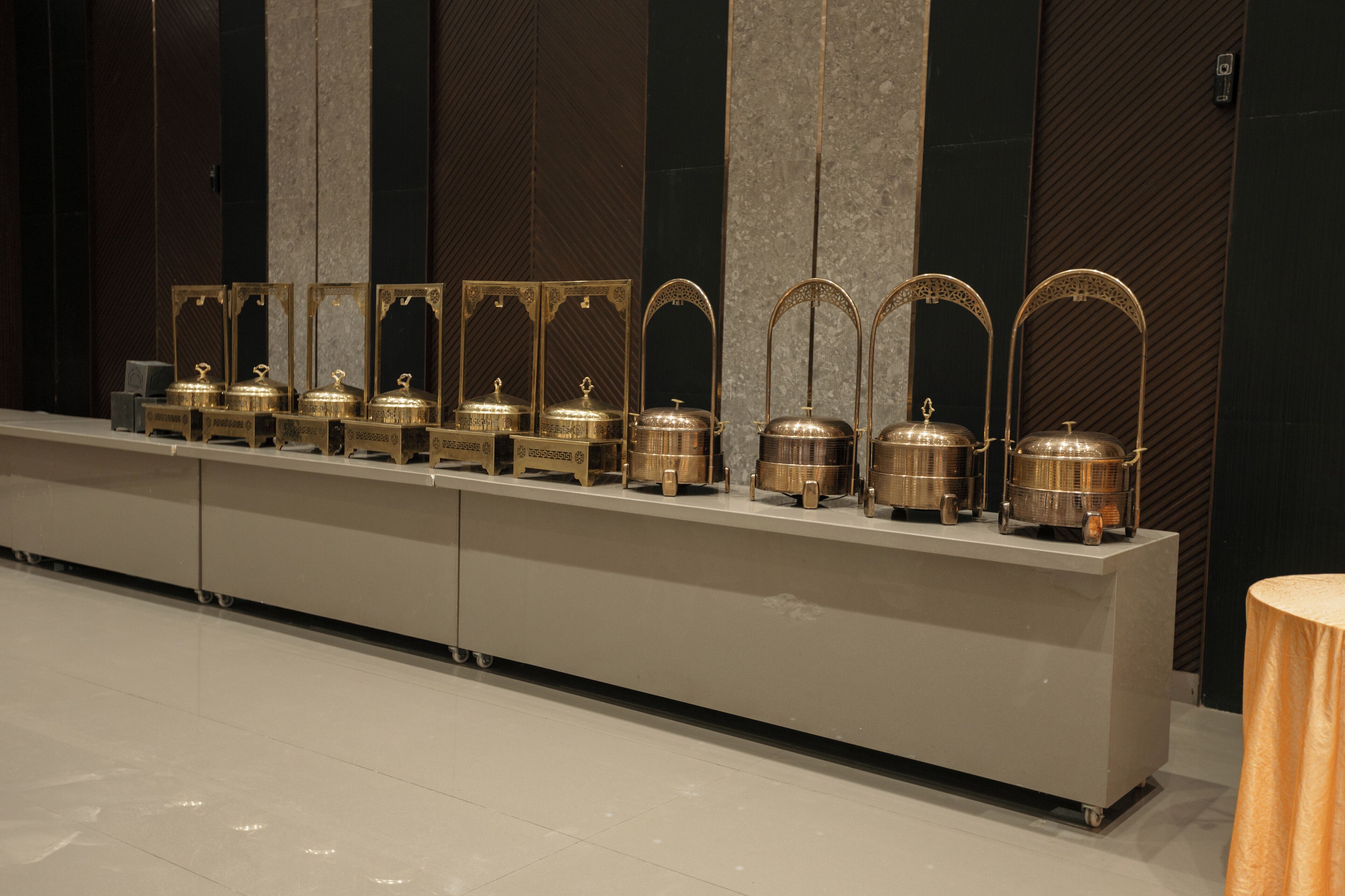 A row of gold-toned, ornate containers on a sleek, modern counter in a hotel lobby.