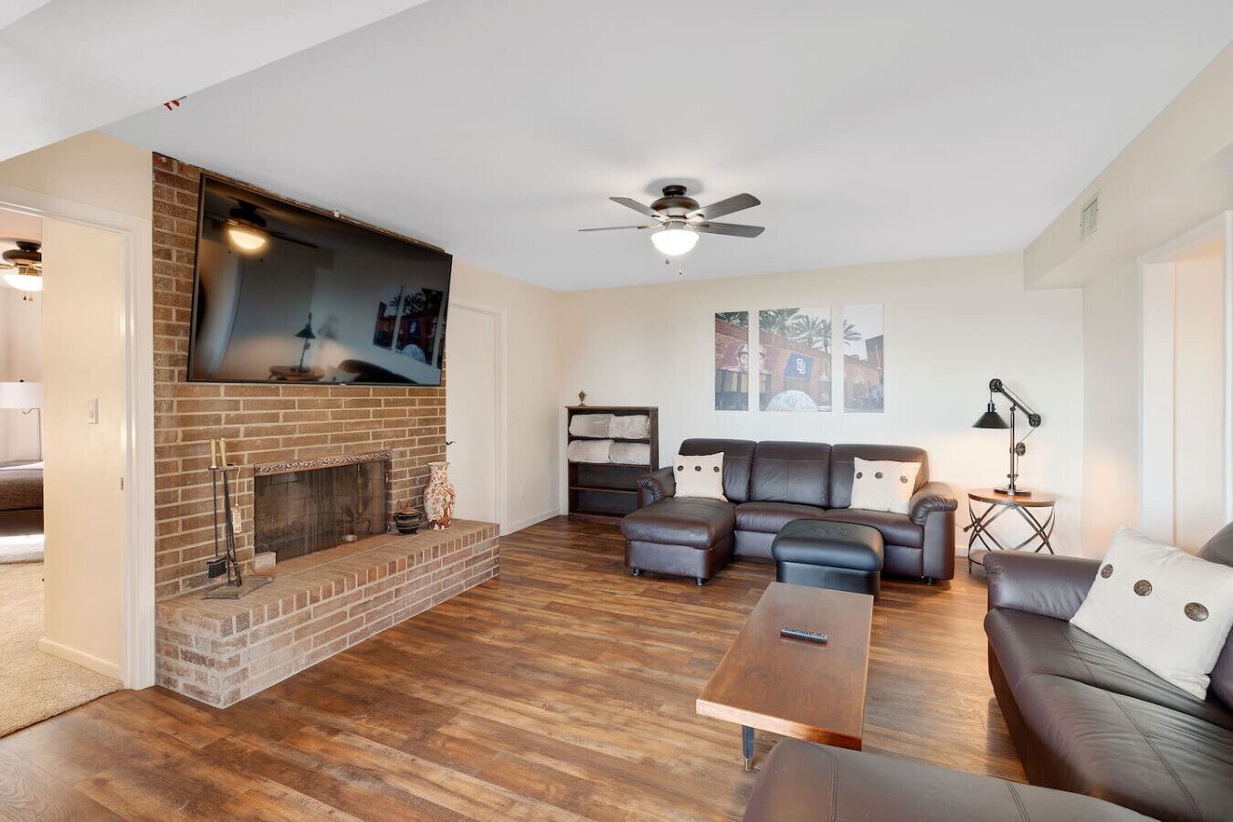 A living room with a brick fireplace, a ceiling fan, a sectional sofa, and a coffee table.