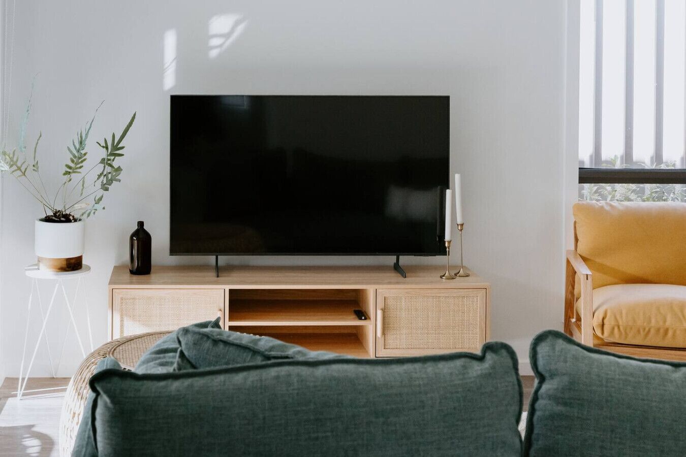 Una sala moderna con un televisor de pantalla plana sobre un mueble de madera, un sofá verde, un sillón amarillo y una pequeña planta en maceta.