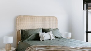 A neatly made bed with a green bedspread and a beige throw blanket, flanked by two bedside lamps and a wicker side table. - Close to town & hospital, quiet & private location (Sale)