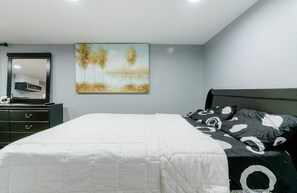 Une chambre à coucher avec un lit, une commode, un miroir et un tableau accroché au mur.