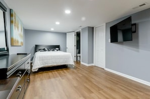 Un dormitorio con cama, cómoda, televisor y obras de arte en la pared.