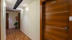 Un pasillo con piso de madera, una puerta con la etiqueta '105' y un extintor en la pared.