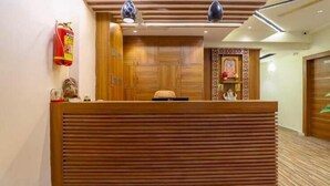 Un área de recepción con un mostrador de madera, dos lámparas colgantes, un extintor y un panel decorativo en la pared.