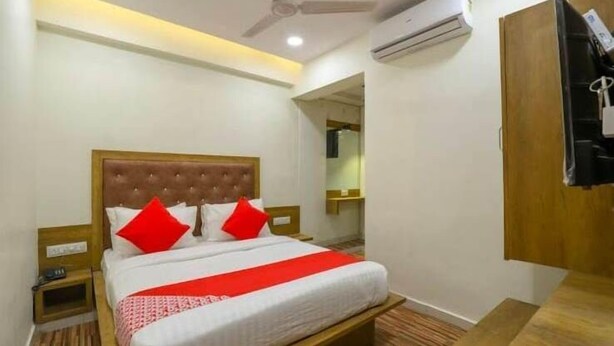 Habitación de hotel con una cama, una mesita de noche de madera, una manta roja y un ventilador de techo, además de un aire acondicionado.
