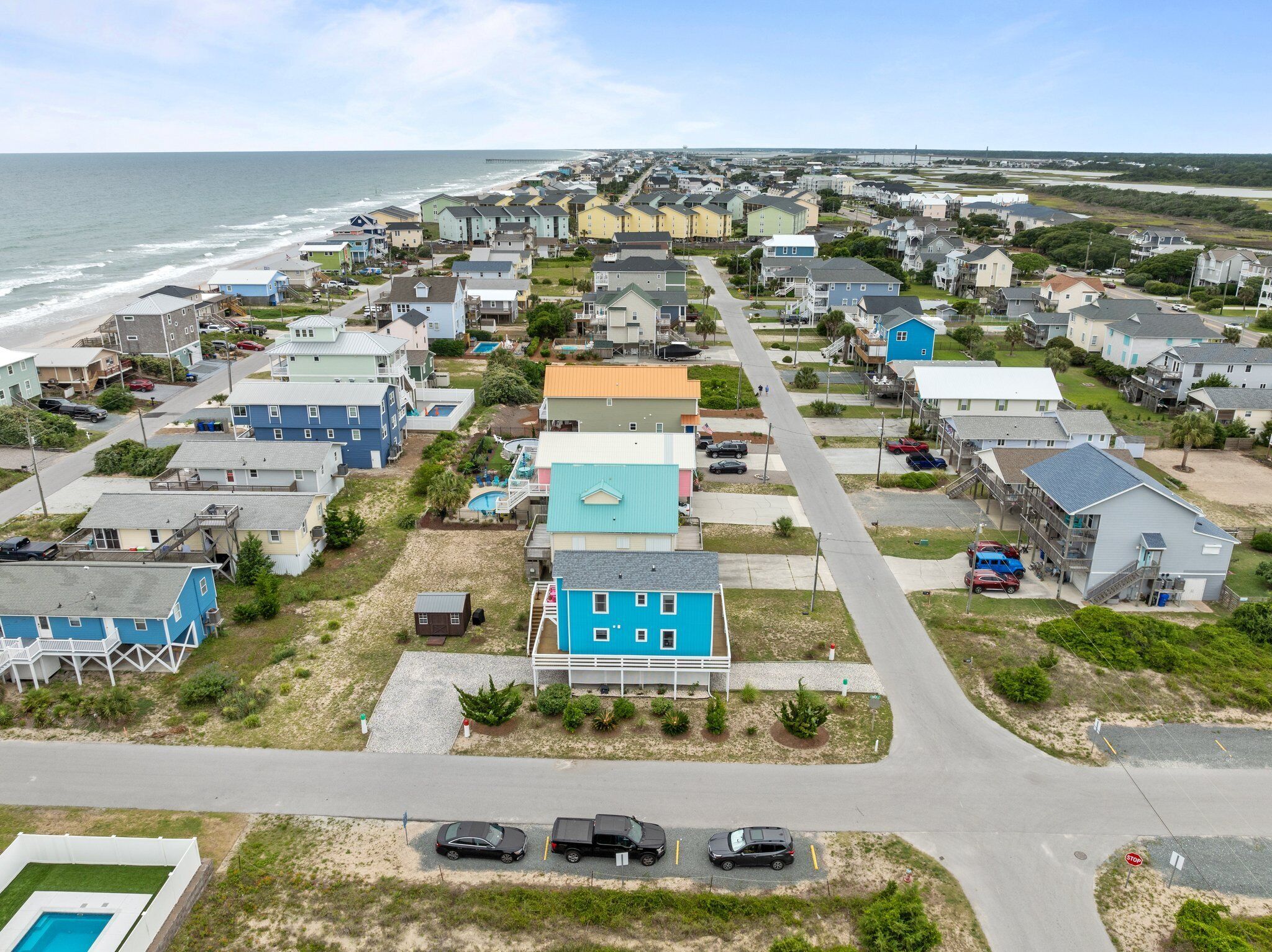 A coastal residential area with houses, a beach, and a pier in the background.