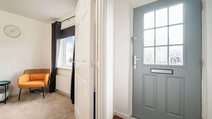 Une pièce avec une porte grise, une fenêtre à vitre dépolie, une chaise et une petite table.