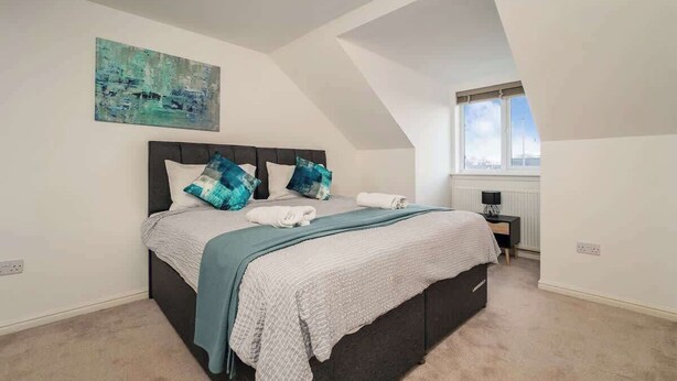 Une chambre à coucher avec un lit, un tableau, une fenêtre et une table de chevet.